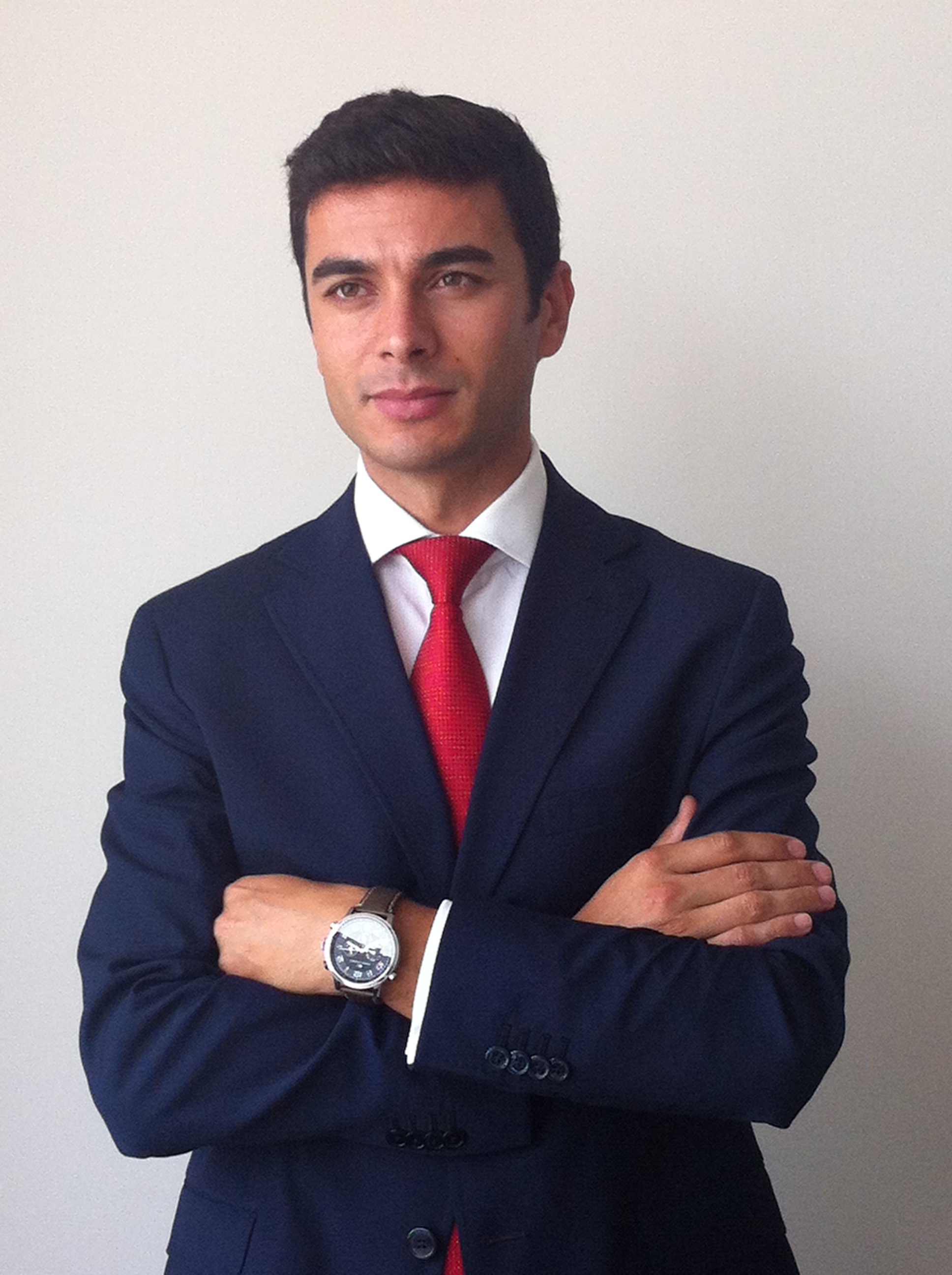 Homem de terno azul e gravata vermelha, braços cruzados.