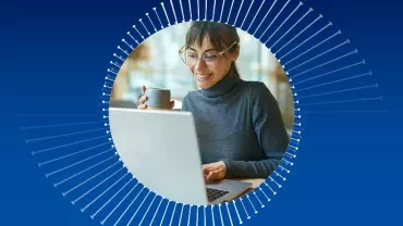 Mulher sorrindo e segurando uma xícara enquanto usa um laptop.