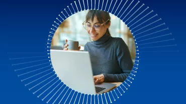 Mulher sorrindo e segurando uma xícara enquanto usa um laptop.