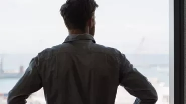 Pessoa olhando pela janela com visão para o mar.