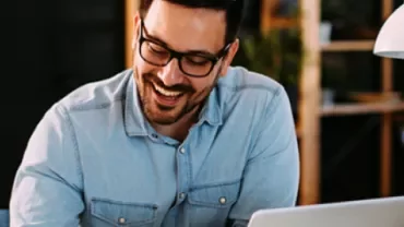 Homem sorrindo enquanto trabalha no laptop.