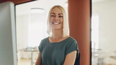 Mulher sorrindo sentada em uma mesa de trabalho.