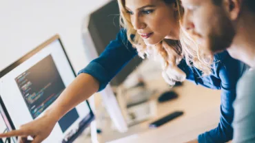 Dois colegas analisam código na tela do computador.