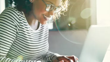 Mulher sorrindo trabalhando em laptop com luz do sol
