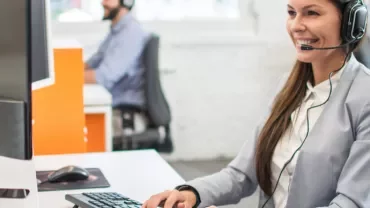 Mulher de fone de ouvido atendendo cliente ao computador.
