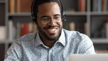 Homem sorrindo usando fones de ouvido, olhando para o laptop.