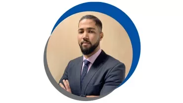 Homem de barba em terno escuro, braços cruzados.