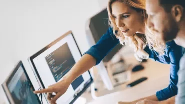 Duas pessoas trabalhando em computadores, colaborando em projeto.