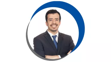 Homem sorridente em terno, fundo branco, circulo azul e cinza.
