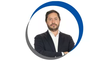 Homem de terno e barba, em fundo branco com círculo azul.