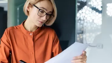 Mulher loira com óculos a ler uma folha de papel 