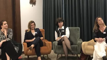 Quatro mulheres sentadas em cadeiras coloridas durante um evento.