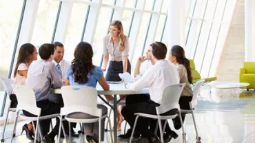 Equipe discutindo em reunião ao redor de mesa em escritório moderno.