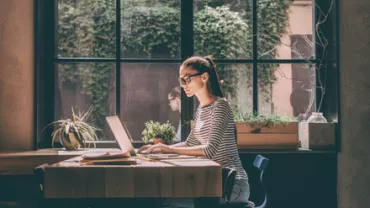 Mulher trabalhando em laptop em um café iluminado pelo sol.