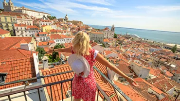 Mulher com chapéu admirando a vista panorâmica de uma cidade costeira ensolarada.