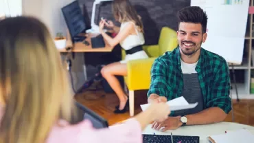 Homem sorridente recebendo documento em escritório moderno.