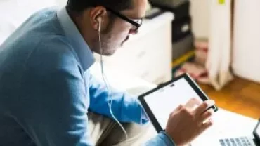 Homem usando fones de ouvido e olhando para um tablet.