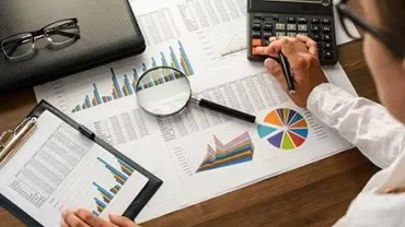 Pessoa analisando gráficos e fazendo cálculos com uma calculadora.