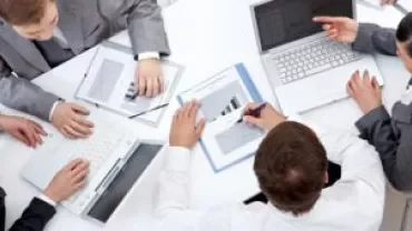 Reunião de negócios com pessoas trabalhando em laptops e gráficos.