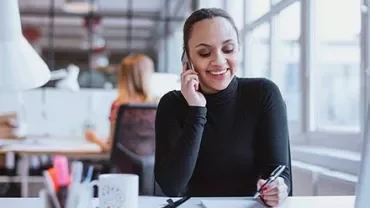 Mulher sorrindo ao telefone em um escritório moderno.
