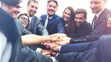Grupo de colegas vestindo ternos formando um círculo e juntando as mãos.