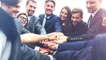 Grupo de colegas vestindo ternos formando um círculo e juntando as mãos.