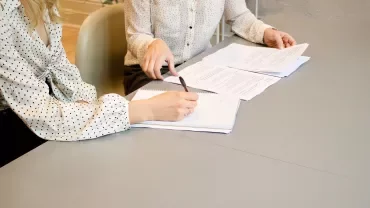 Duas pessoas revisando documentos na mesa.