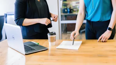 Duas pessoas discutem em frente a um laptop em uma mesa de escritório.