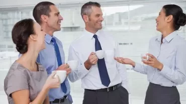 Grupo de colegas rindo e conversando durante um intervalo para café no escritório.