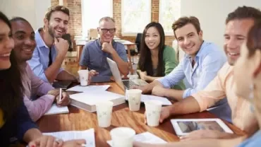 Grupo de pessoas sorrindo em uma reunião ao redor de uma mesa.