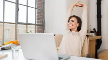 Mulher sorrindo e espreguiçando-se em frente ao laptop.