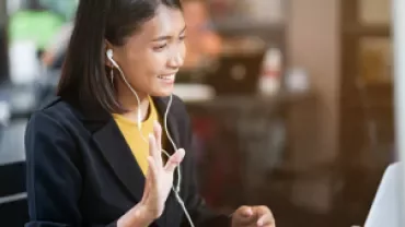 Mulher sorrindo e participando de reunião online com fones de ouvido.