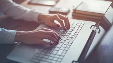 Pessoa digitando em laptop em mesa de madeira.
