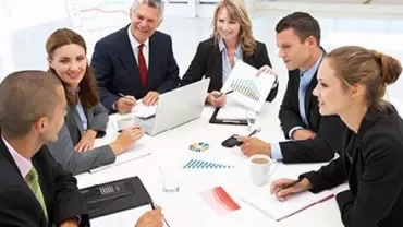 Reunião de negócios com pessoas ao redor de uma mesa, gráficos e laptop.