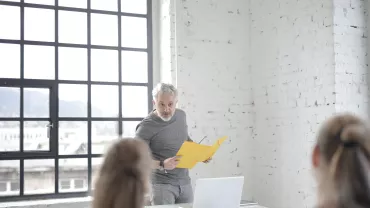 Homem apresentando papel amarelo em escritório moderno.