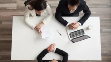 Pessoa em entrevista de emprego sentada à mesa com dois recrutadores.