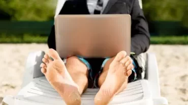 Homem de terno trabalhando em um laptop sentado na praia.