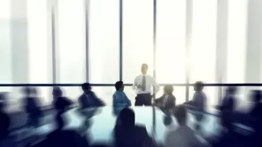 Reunião de negócios com pessoas ao redor de uma mesa em sala iluminada.