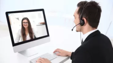 Homem com fone de ouvido em videoconferência com mulher em computador.