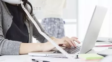 Mulher digitando no laptop, usando telefone no escritório.