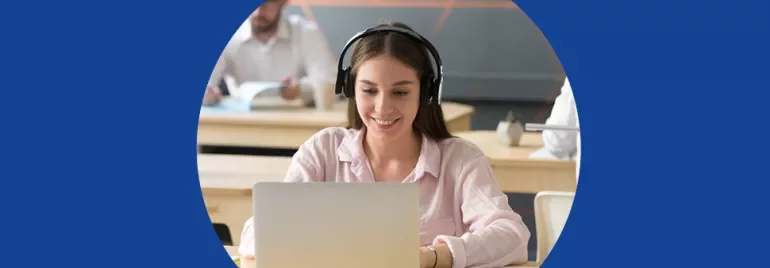 Mulher usando fones e laptop em sala de aula.