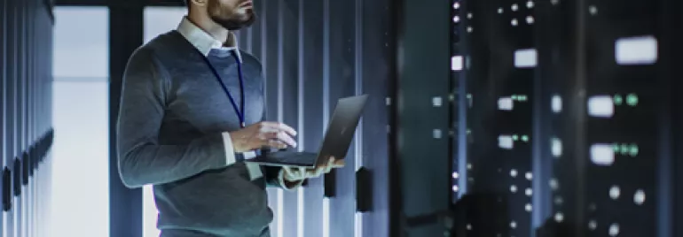 Homem usando laptop em data center moderno.