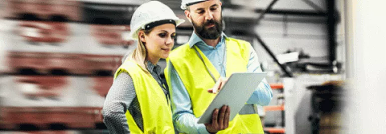 Dois trabalhadores de colete refletivo verificam um tablet em um armazém.