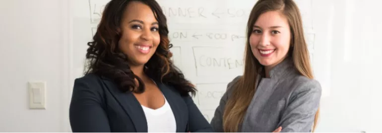 Duas mulheres sorridentes em frente a um quadro branco.