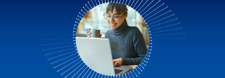 Mulher sorrindo e segurando uma xícara enquanto usa um laptop.