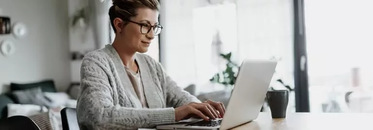 Pessoa usando laptop em casa com uma xícara ao lado.