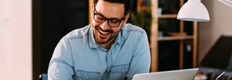 Homem sorrindo enquanto trabalha no laptop.