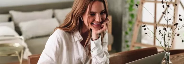 Mulher sorrindo enquanto usa laptop em casa.