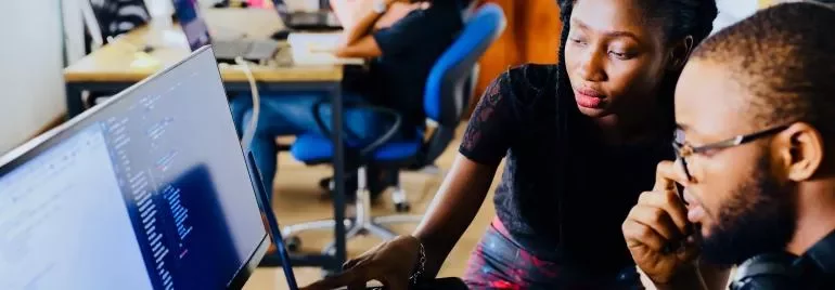 Duas pessoas trabalhando em frente a um computador em um escritório.
