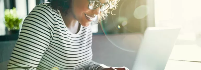 Mulher sorrindo trabalhando em laptop com luz do sol